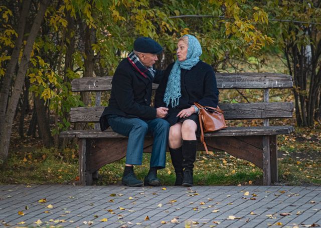 older couple sitting on bench talking warmly autumn park